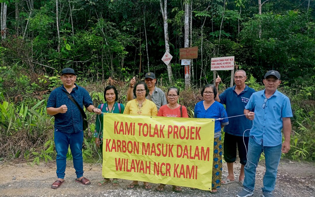Community members hold a sign that says "kami tolak projek karbon masuk dalam wilayah ncr kami"